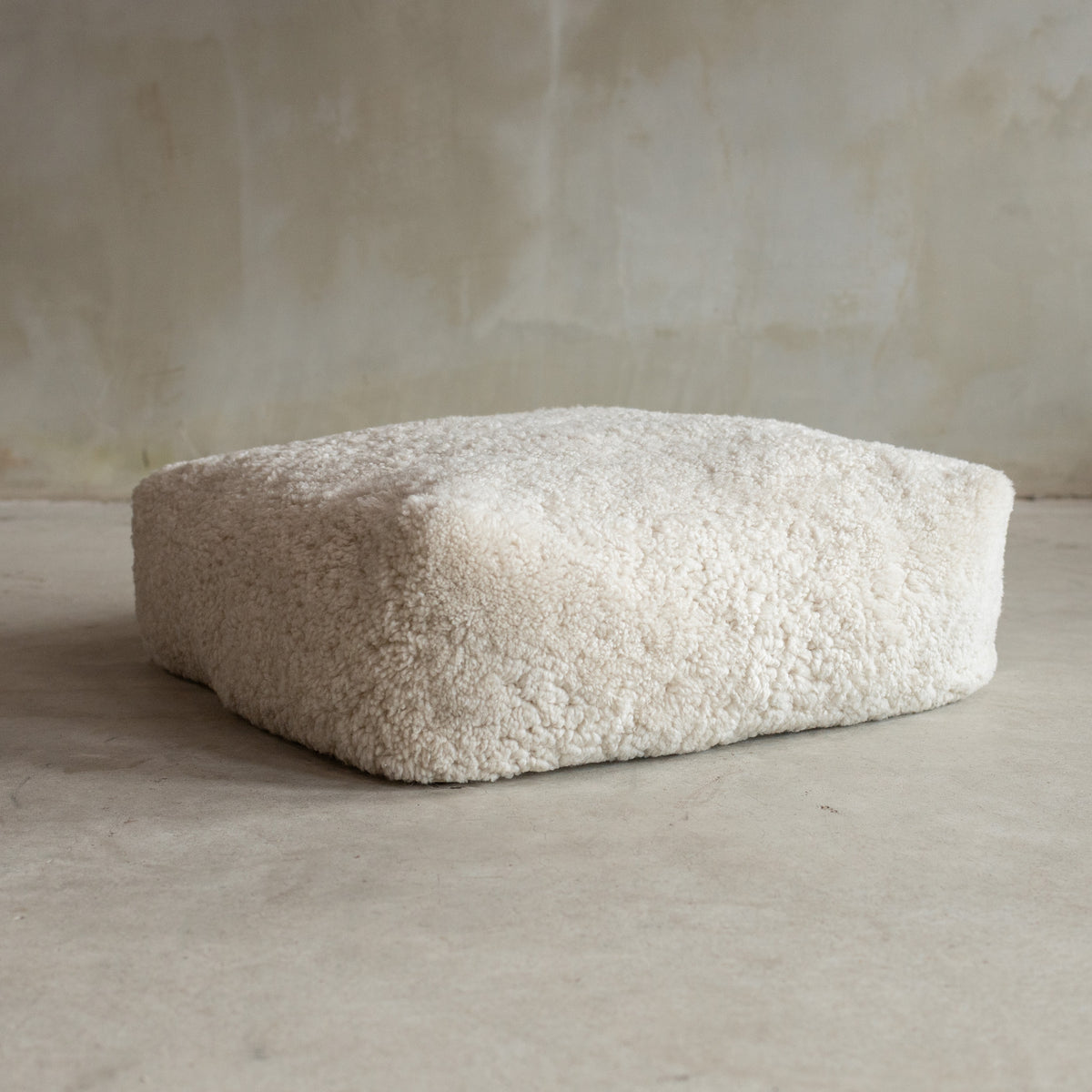 Coussin de sol peau de mouton bouclée blanc cassé 65x65x20 cm posé au sol, effet teddy