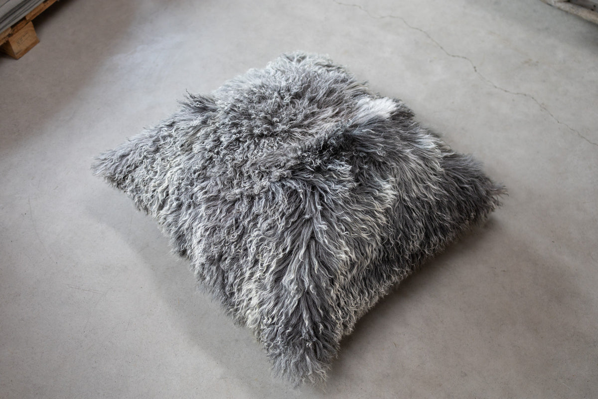 Grand coussin de sol en peau de mouton bouclée gris naturel posé par terre