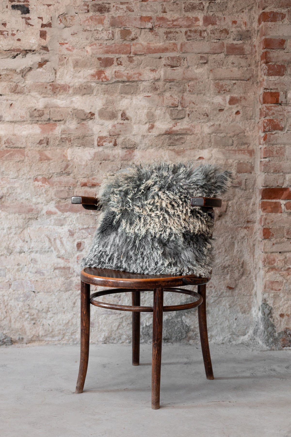 Coussin en peau de mouton du Tibet gris naturel posé sur une chaise en bois