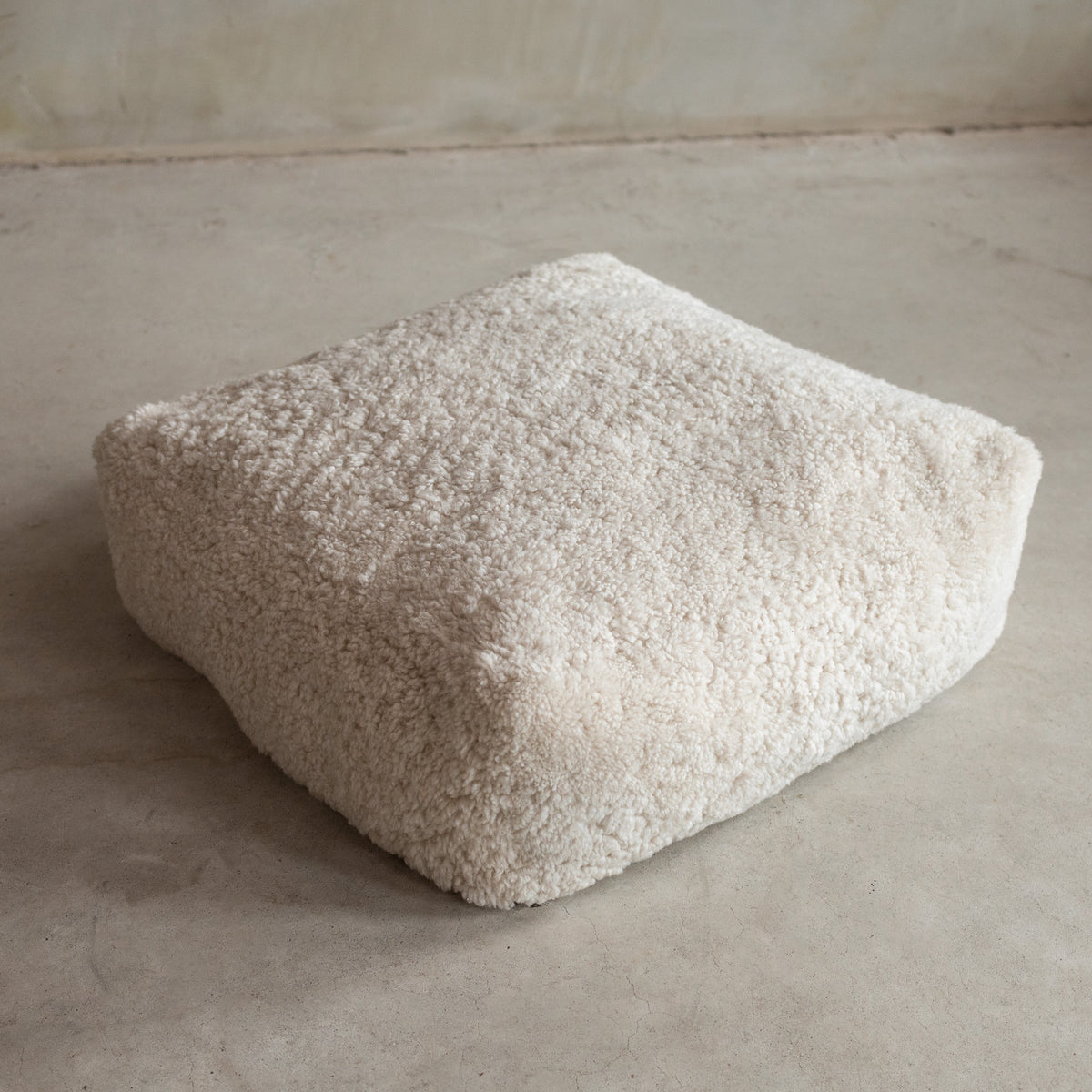 Coussin de sol peau de mouton bouclée blanc cassé vu de trois quarts, boucles naturelles denses