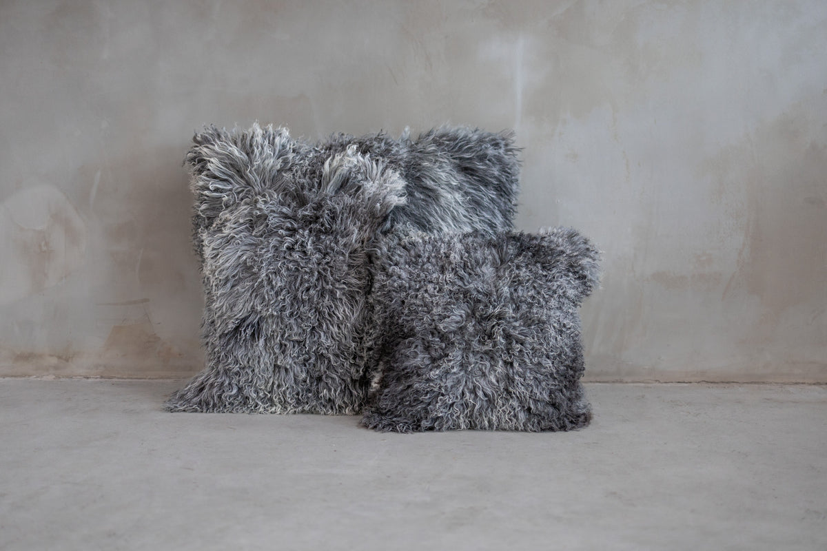 Coussin de sol 80x80 cm et coussin 45x45 cm en peau de mouton du Tibet gris naturel contre un mur