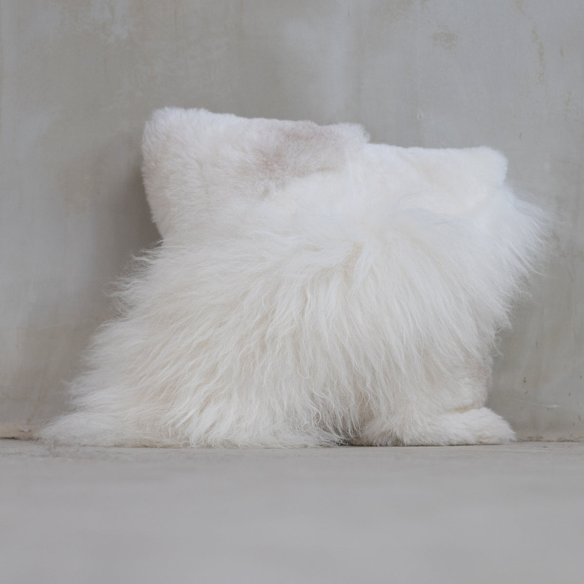 Coussins patchwork en peau de mouton blanc posés au sol contre un mur