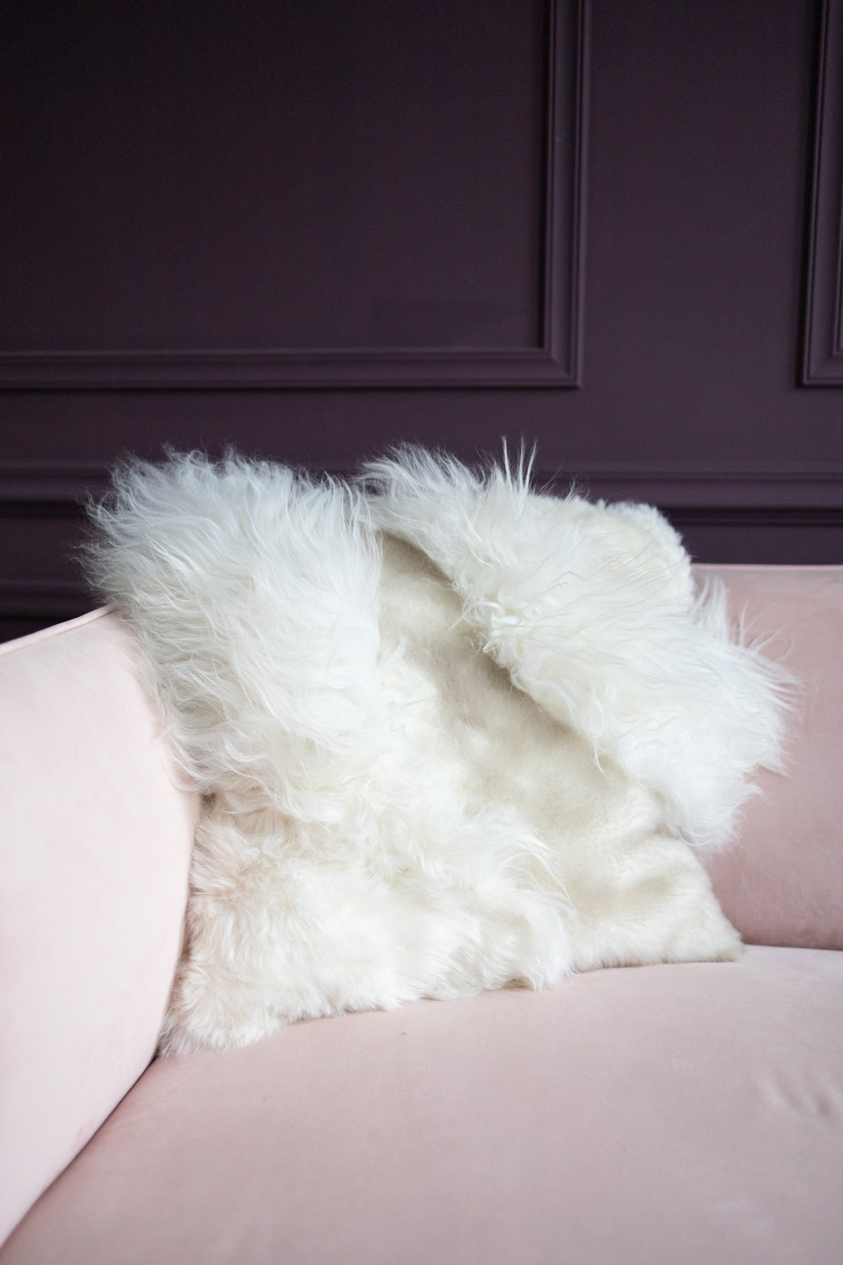 Coussin patchwork en peau de mouton blanc posé sur un canapé rose poudré