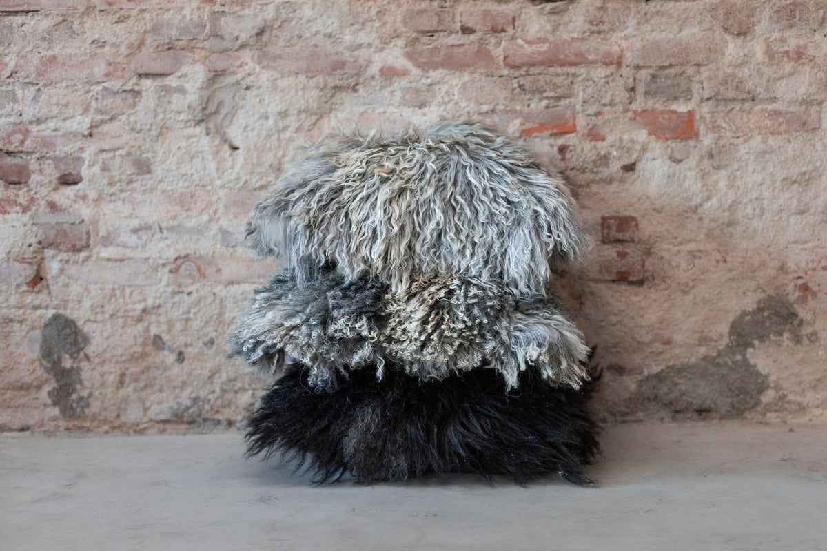 Pile de coussins en peau de mouton gris naturel devant un mur de briques